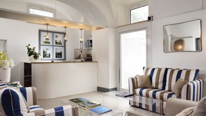 Un salon moderne avec un canapé à rayures, une table basse en verre et un coin cuisine doté d’un plan de travail blanc et de luminaires suspendus.