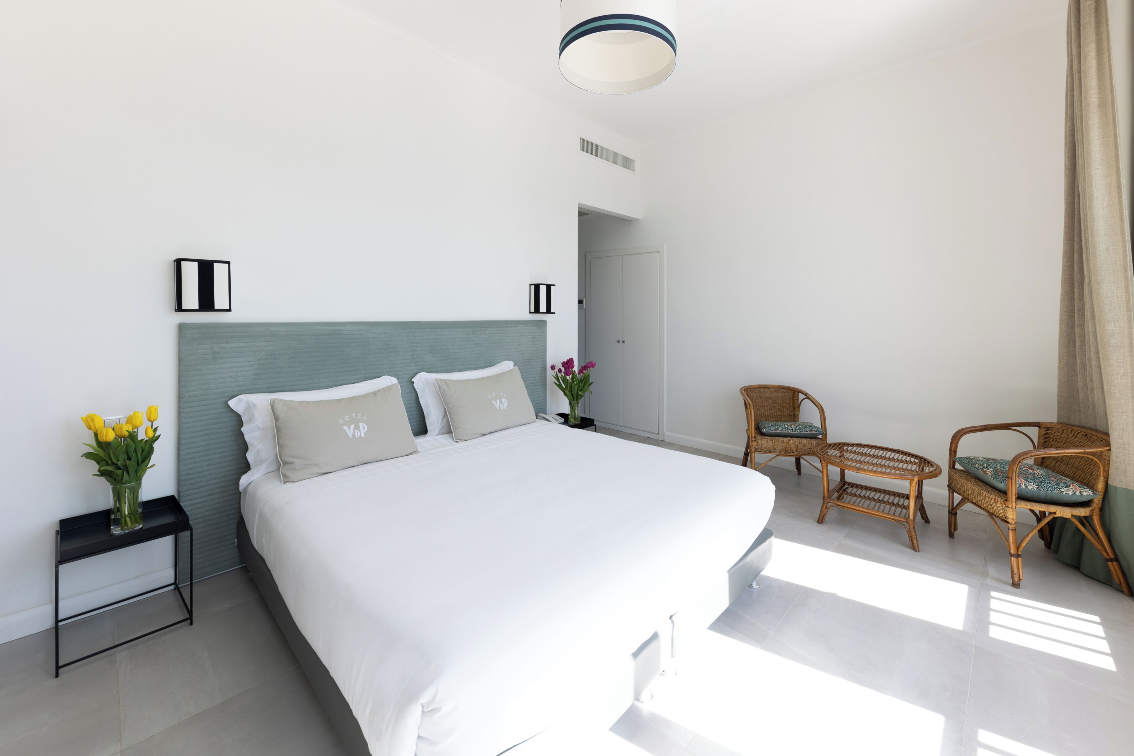 Una habitación de hotel moderna con una cama grande, dos mesitas de noche, una pequeña mesa y dos sillas de mimbre.