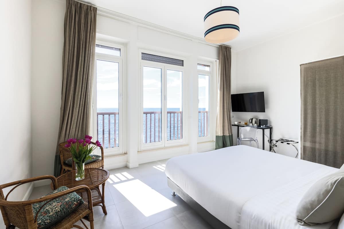 A hotel room with a bed, a TV, a desk, and a view of the sea.