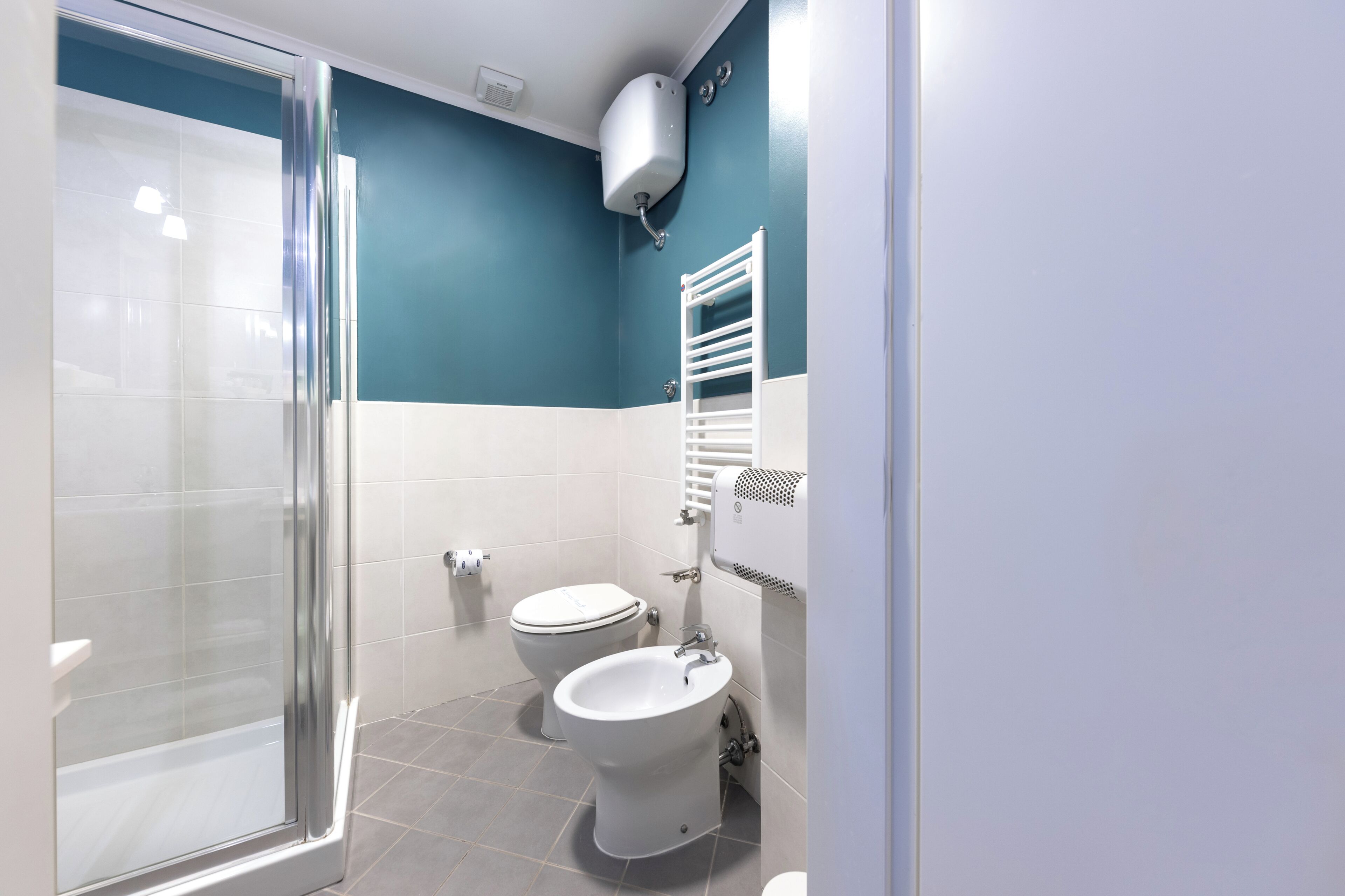 A bathroom with a glass shower enclosure, two toilets, and a towel rack.