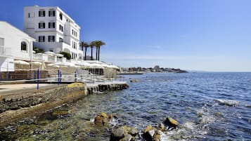 A coastal building with balconies, a rocky shoreline, and clear blue water.