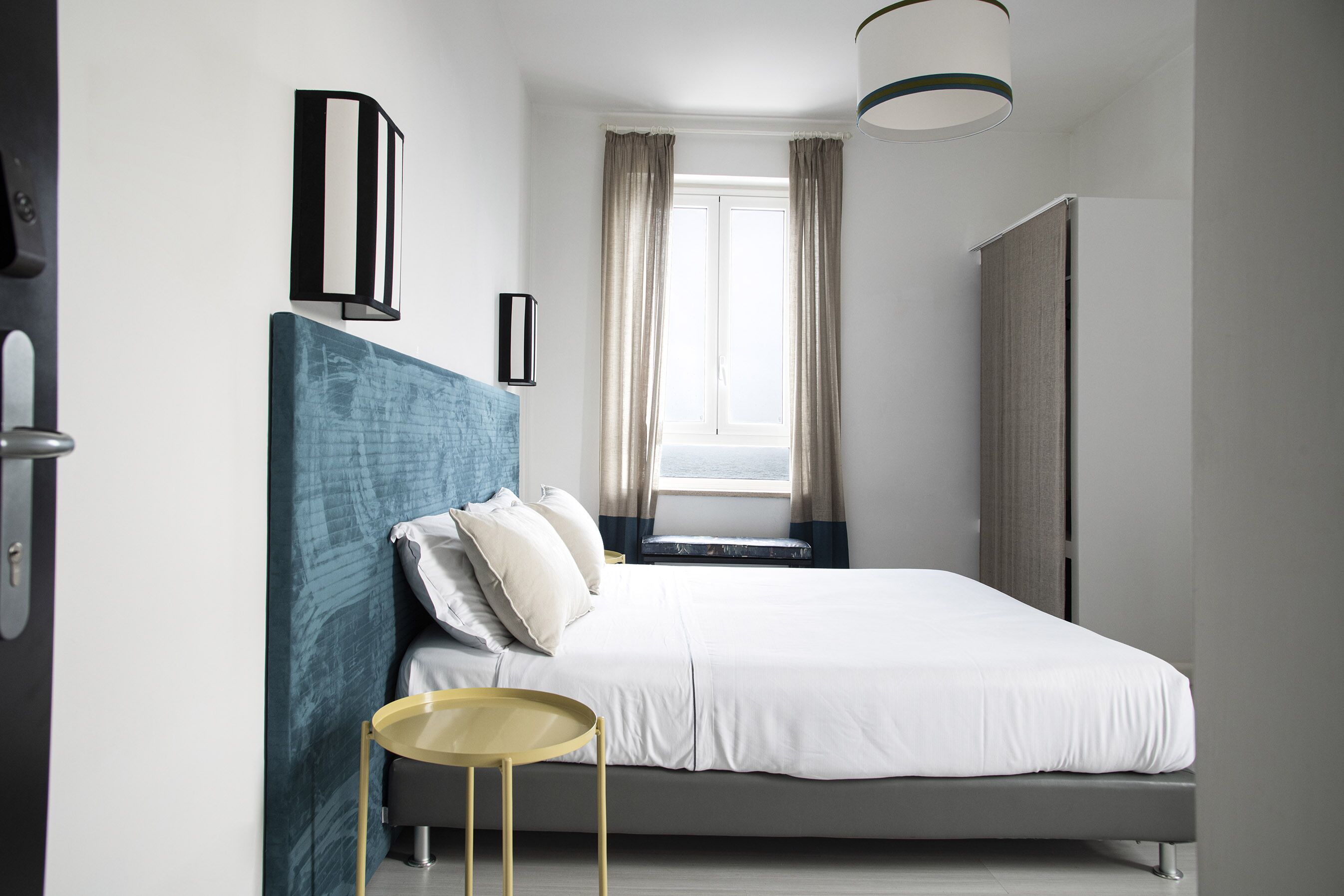 Une chambre à coucher moderne, avec un lit, des tables de chevet, une fenêtre avec des rideaux et un luminaire au plafond.