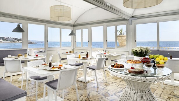 Un espace de restauration lumineux, avec des meubles blancs et de grandes fenêtres donnant sur la mer.