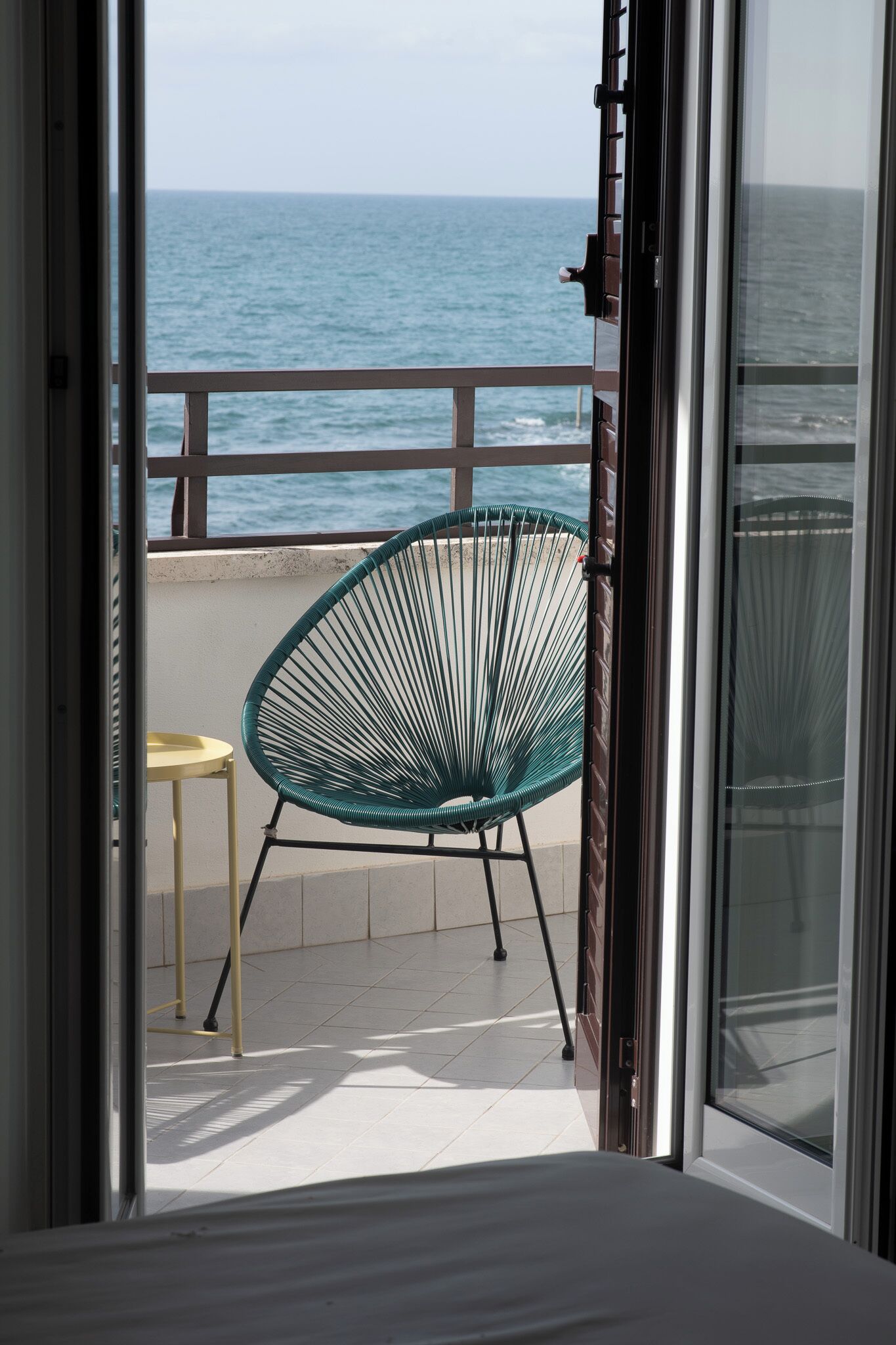 Een balkon met uitzicht op zee, een groene stoel en een klein tafeltje.