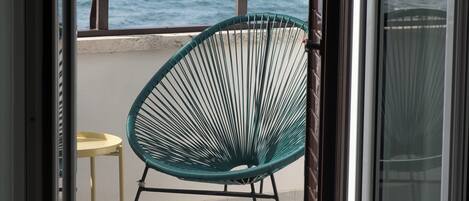 A balcony with a view of the sea, a green chair, and a small table.