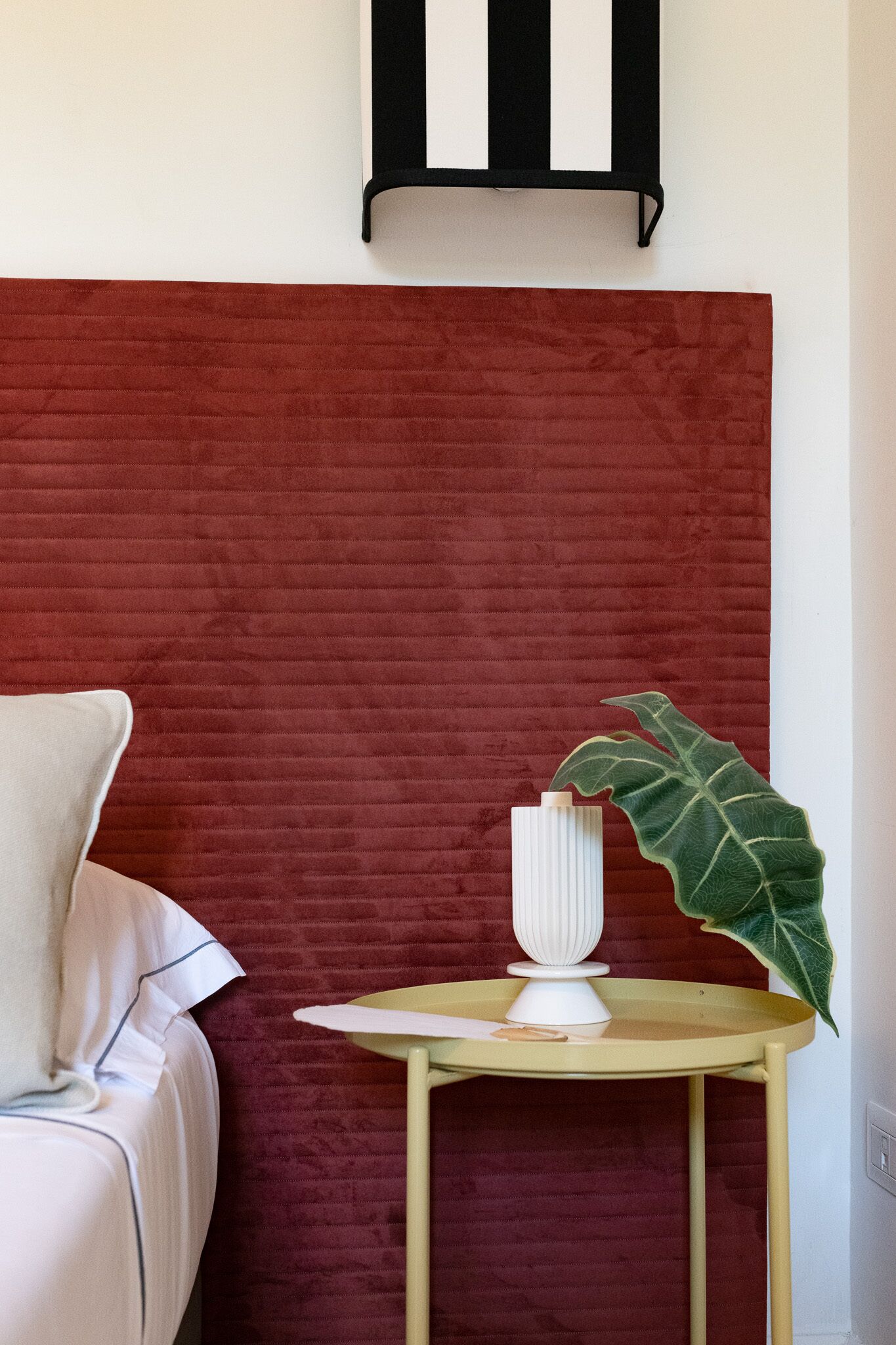Una habitación con una pared roja con textura, una silla blanca, una mesita redonda con un jarrón blanco y una planta verde grande.