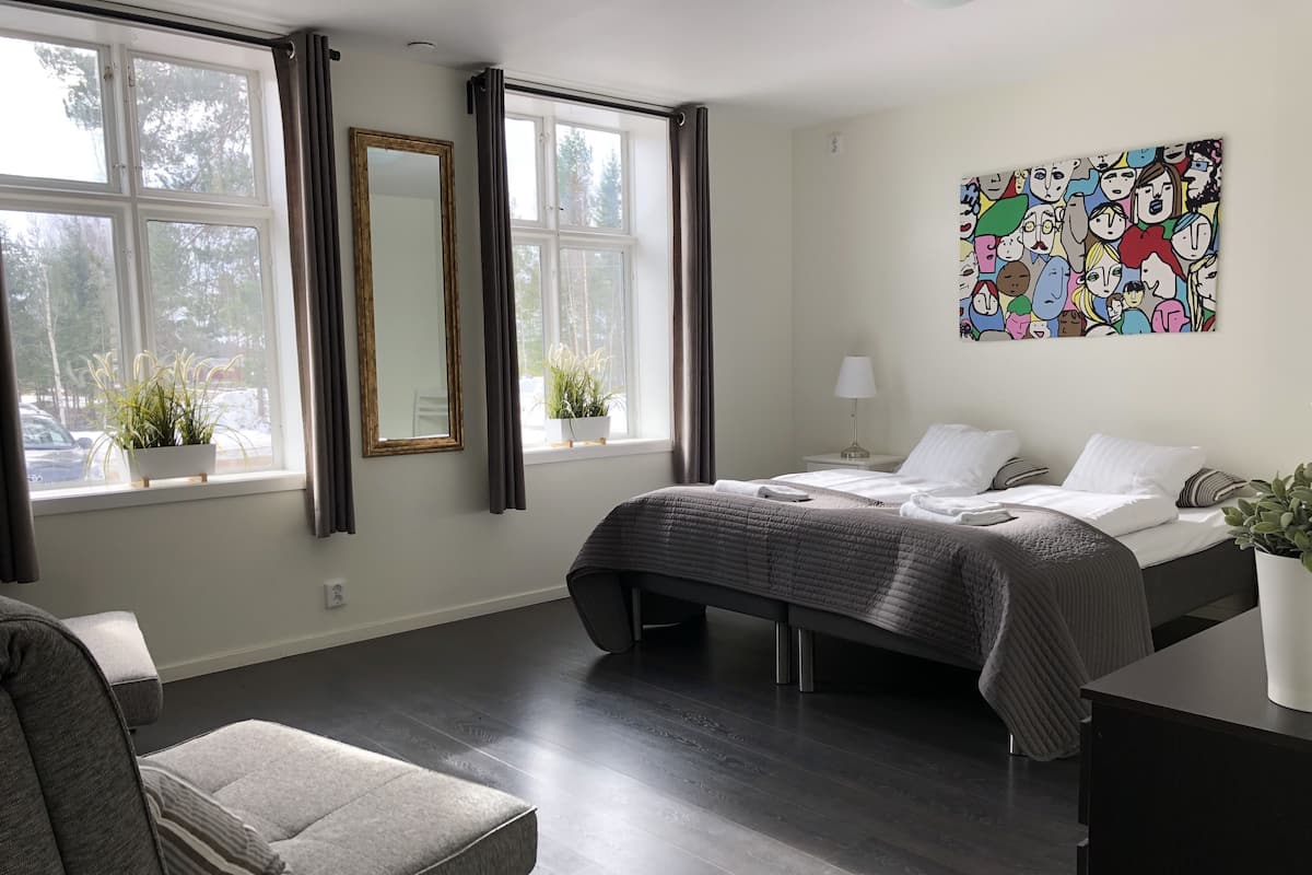 A modern hotel room with a bed, bedside table, lamp, and a colorful artwork on the wall.