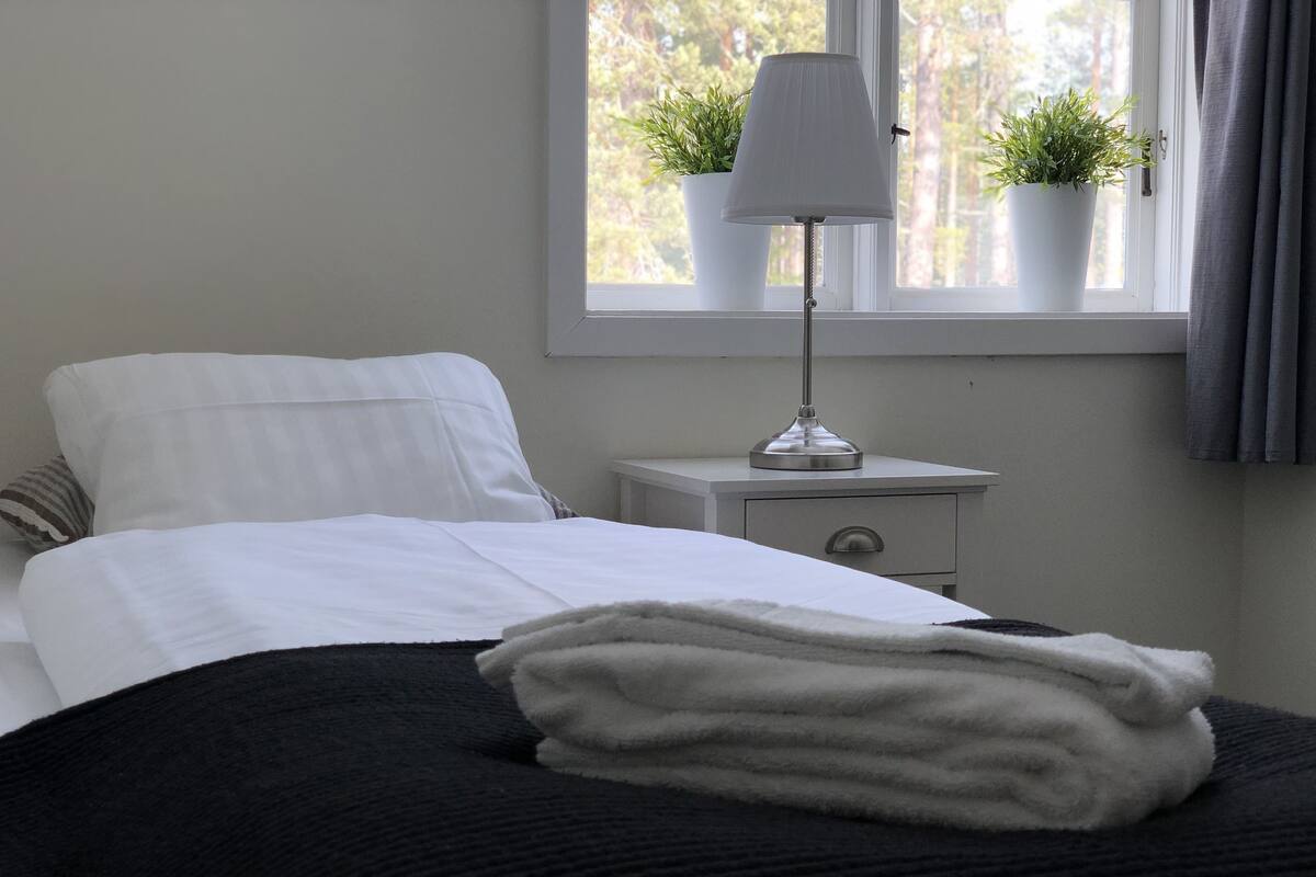 A neatly made bed with a black and white duvet, a bedside lamp, and two potted plants on a windowsill.