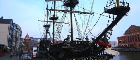 A tall ship docked at a pier with a cityscape in the background.