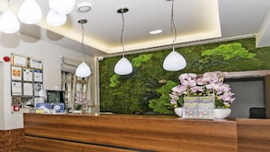 Un comptoir d’accueil avec un plan de travail en bois, des suspensions blanches, un mur végétal recouvert de mousse verte et une composition florale avec des orchidées en pot.