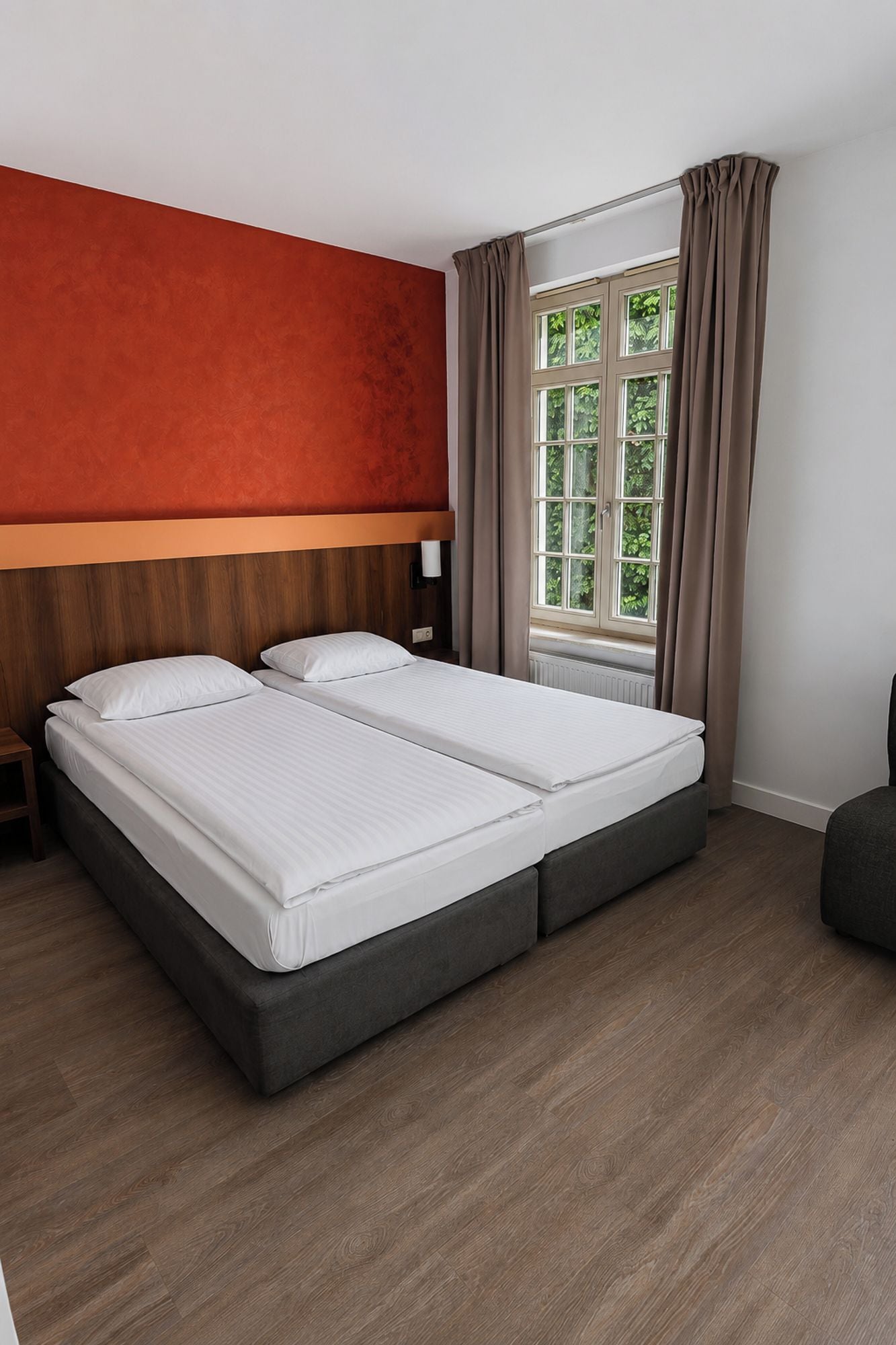 A double bed with a wooden headboard, a nightstand, and a window with curtains.
