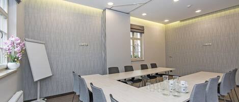 A conference room with a long table, grey chairs, a whiteboard, and a projector on the ceiling.