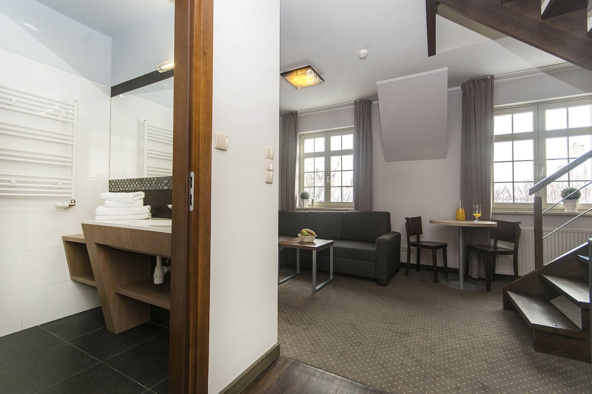Une chambre d’hôtel moderne comprenant une salle de bain, un espace de vie avec un canapé et une petite table, ainsi qu’un escalier.