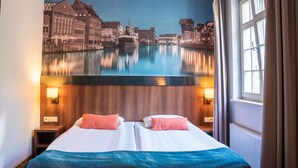 Une chambre d’hôtel avec un lit, deux oreillers, une table de chevet et une fresque murale représentant un paysage de canal.
