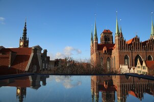 A historic building with a clock tower and spires, reflected in a calm body of water.