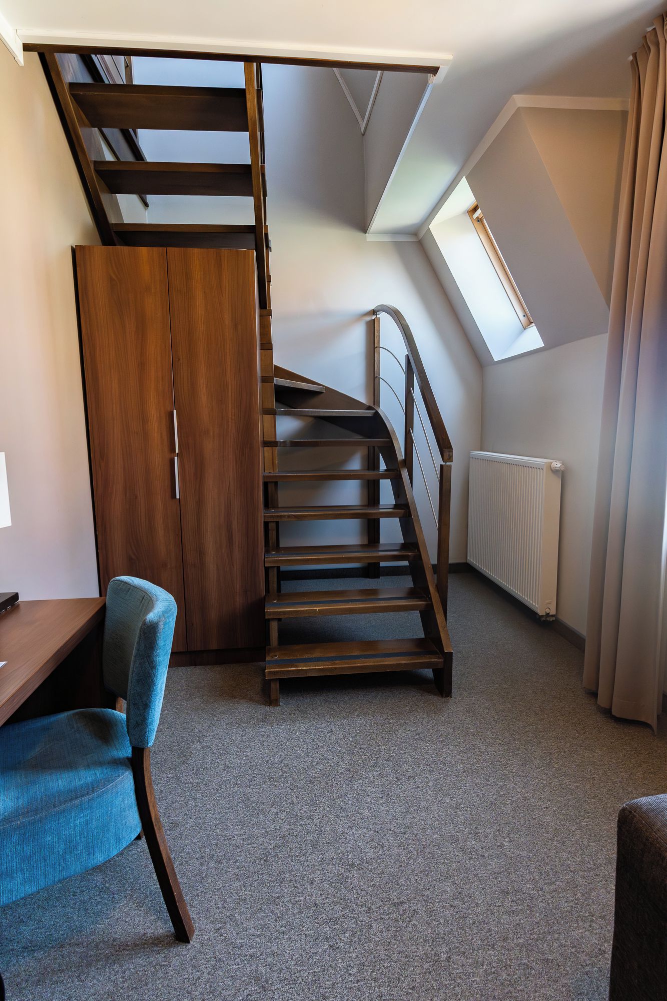 Une pièce avec un escalier en bois, un bureau, une chaise et un radiateur.