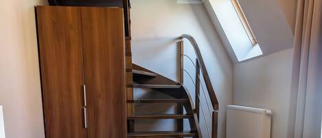 A room with a wooden staircase, a desk, a chair, and a radiator.