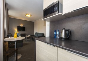 A compact hotel room with a kitchenette, a dining area, and a seating area.
