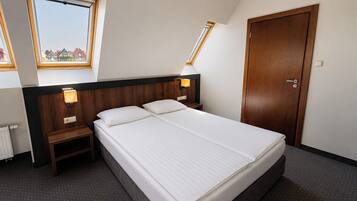 A hotel room with a large bed, two bedside tables, a wooden wardrobe, and a window with a view of buildings.
