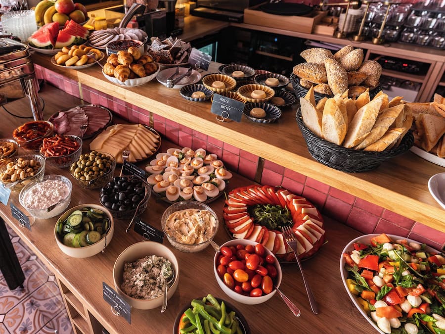 Una mesa de buffet con diversas opciones de comida, como pan, frutas, quesos y ensaladas.
