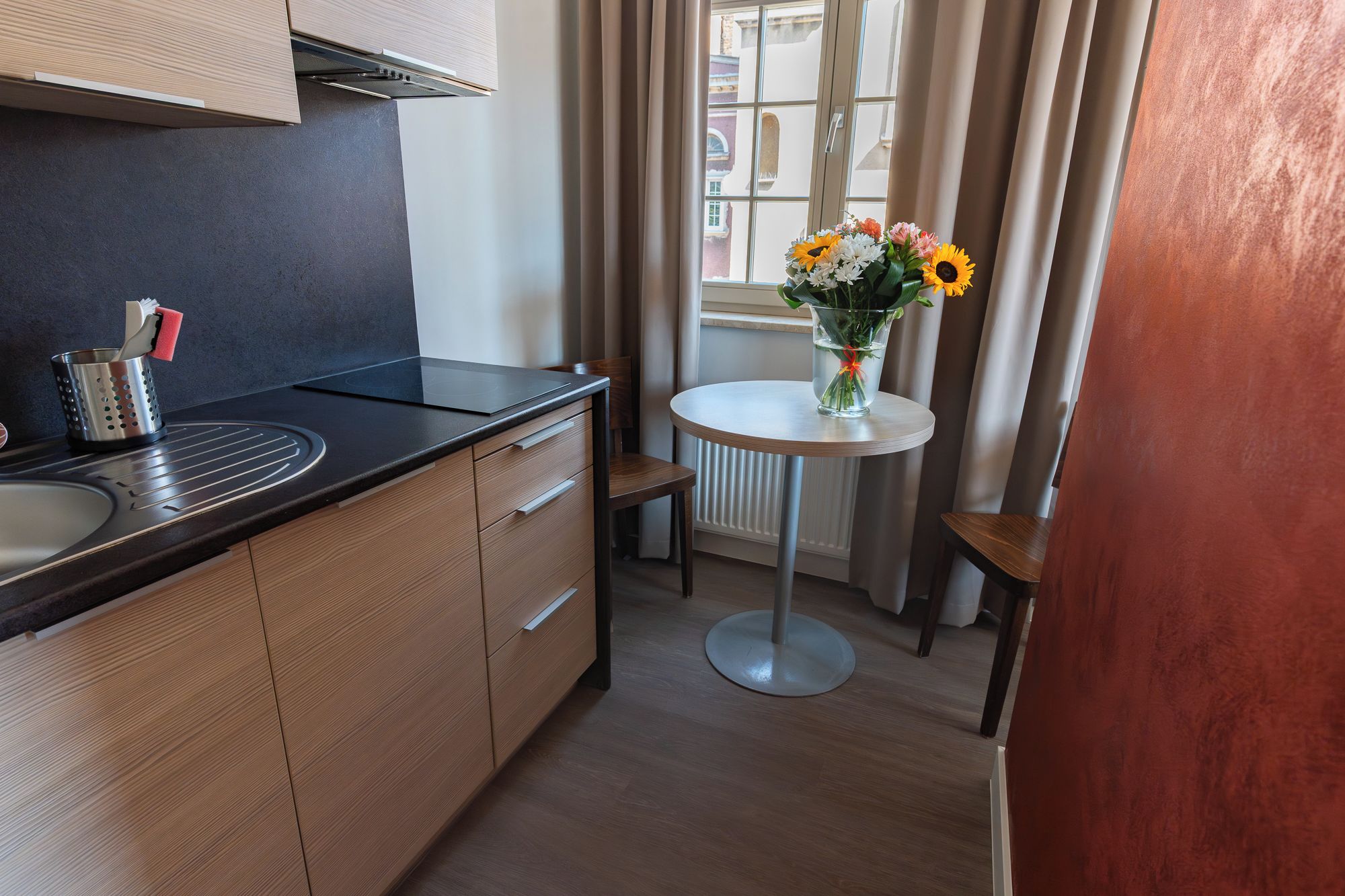 A compact kitchen with a modern stove, a sink, and a small round table with a vase of flowers.