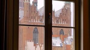 Une fenêtre à quatre carreaux, chacun offrant une vue sur un bâtiment historique doté d’une tour imposante.