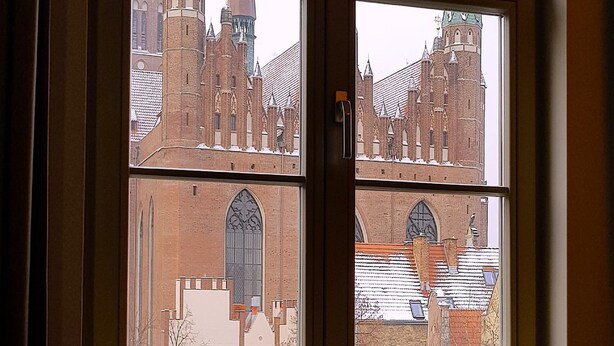 A window with four panes, each offering a view of a historic building with a prominent tower. - Apart Neptun (Gdansk)