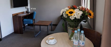 A hotel room with a round table, a chair, a desk with a chair, a flat-screen TV, and a window with curtains.