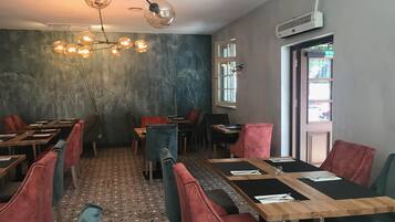 A restaurant interior with round tables, red upholstered chairs, a patterned floor, and a modern chandelier.