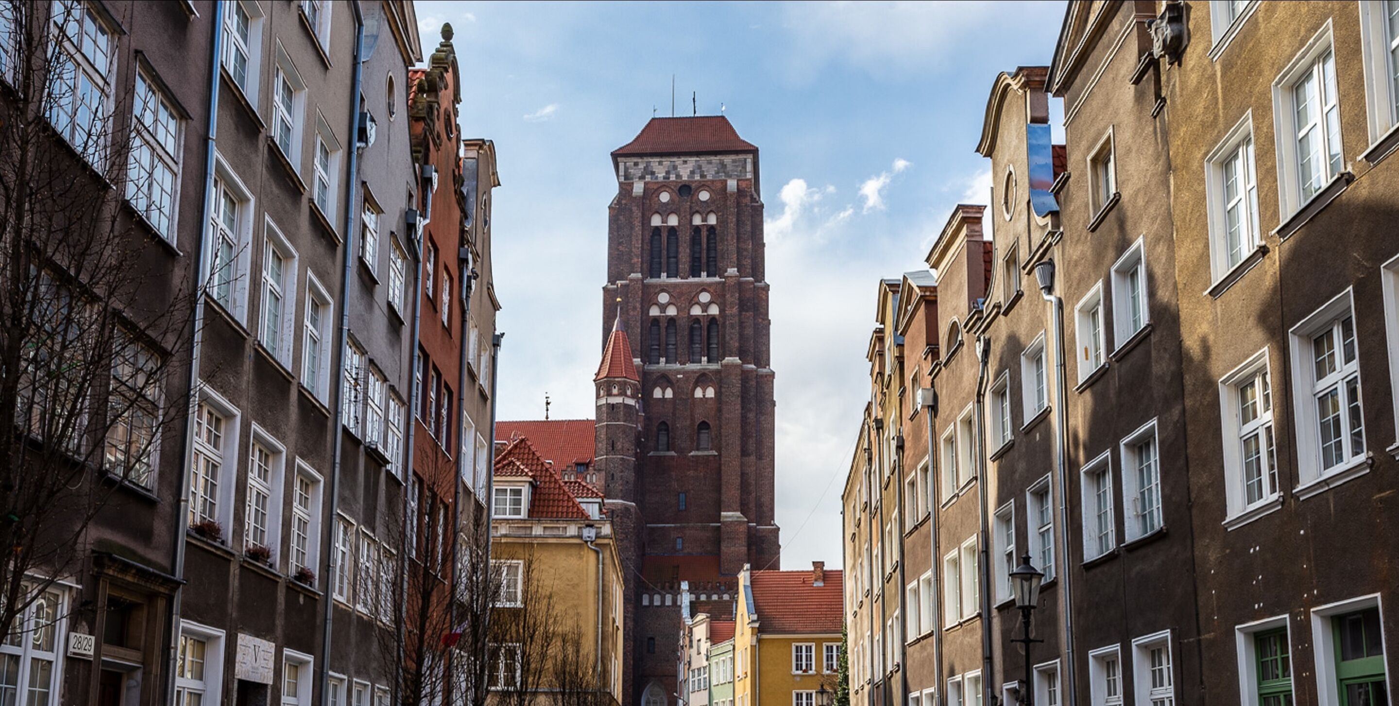 A narrow street lined with historic buildings, a prominent tower, and a church steeple.