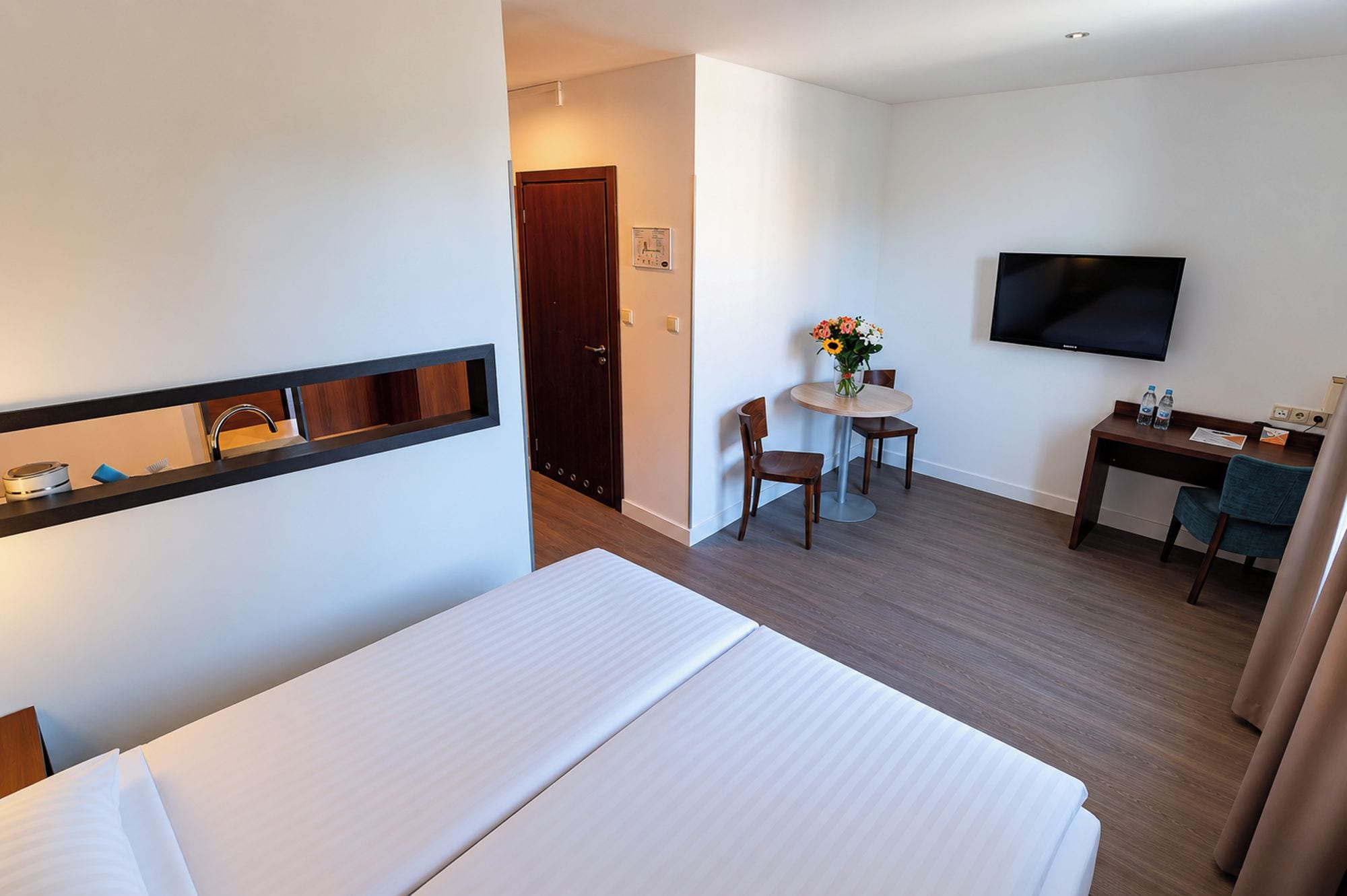 Habitación de hotel con una cama, un escritorio, una silla, un televisor y una mesita con un florero.