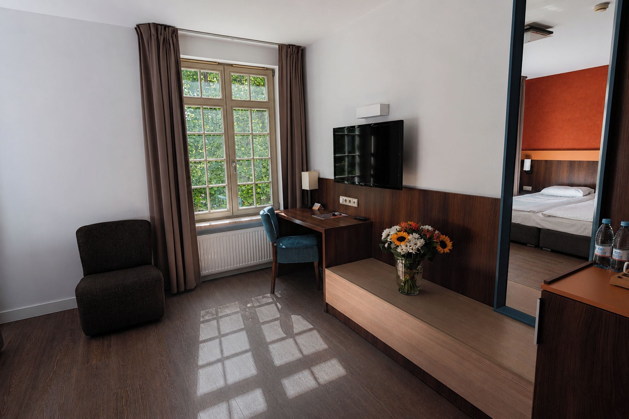 A hotel room with a bed, a desk, a chair, a TV, and a window with curtains.