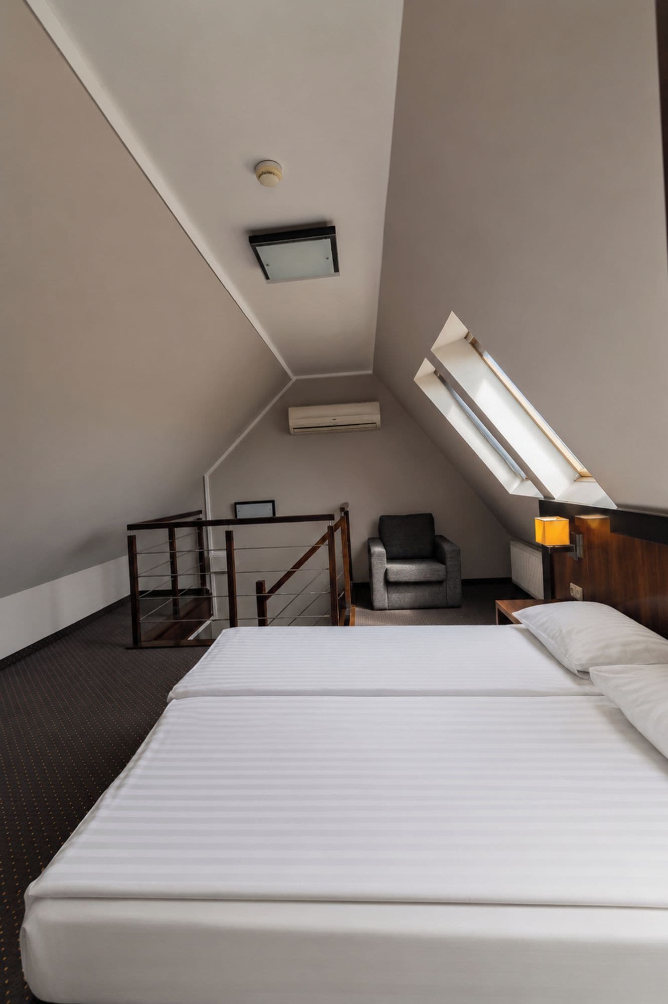 Una habitación de hotel con una cama, una silla, un escritorio y un tragaluz.