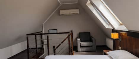 Una habitación de hotel con una cama, una silla, un escritorio y un tragaluz.