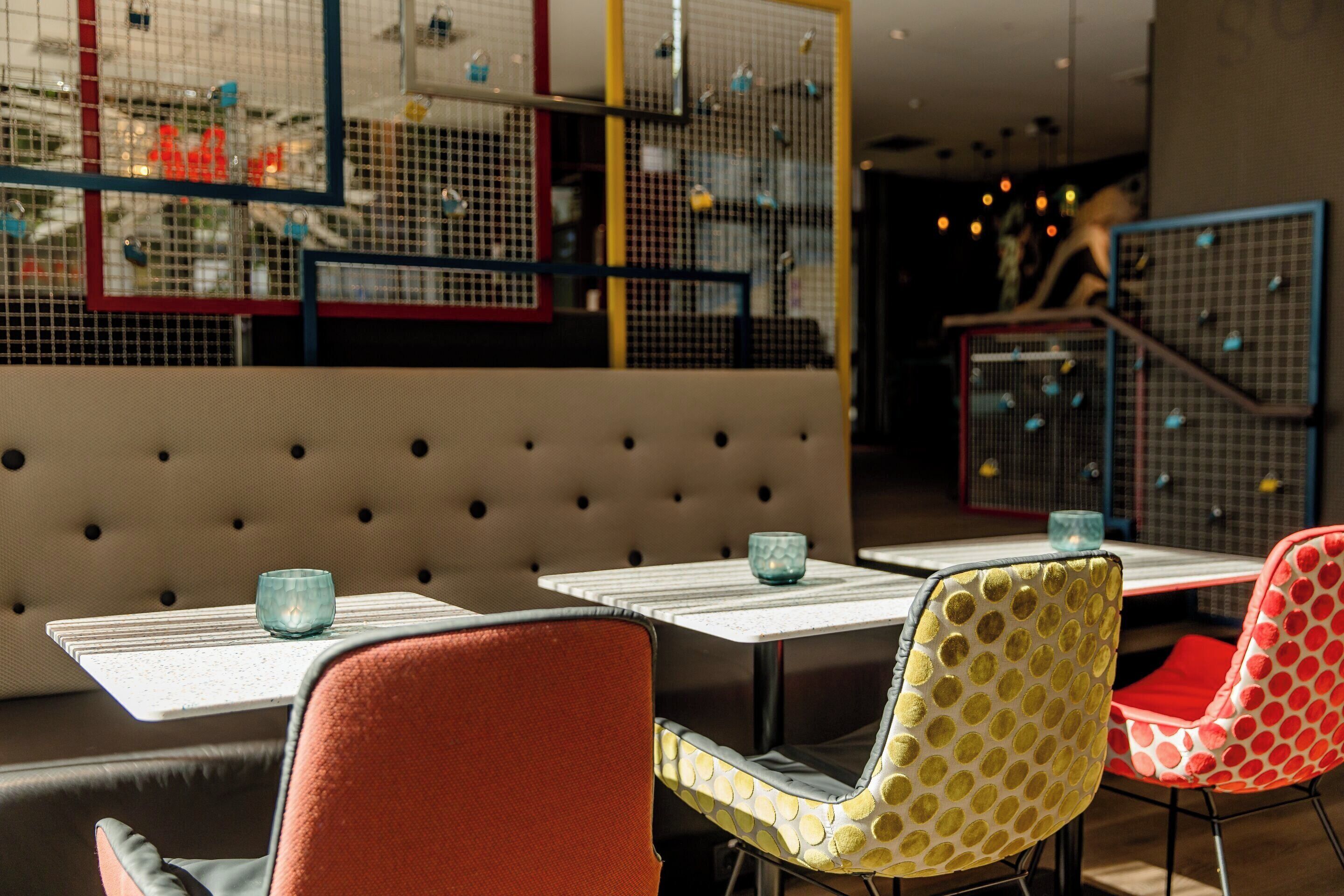 A restaurant interior with a booth seating area, tables with glass tops, and colorful chairs.