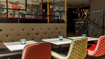 A restaurant interior with a booth seating area, tables with glass tops, and colorful chairs.