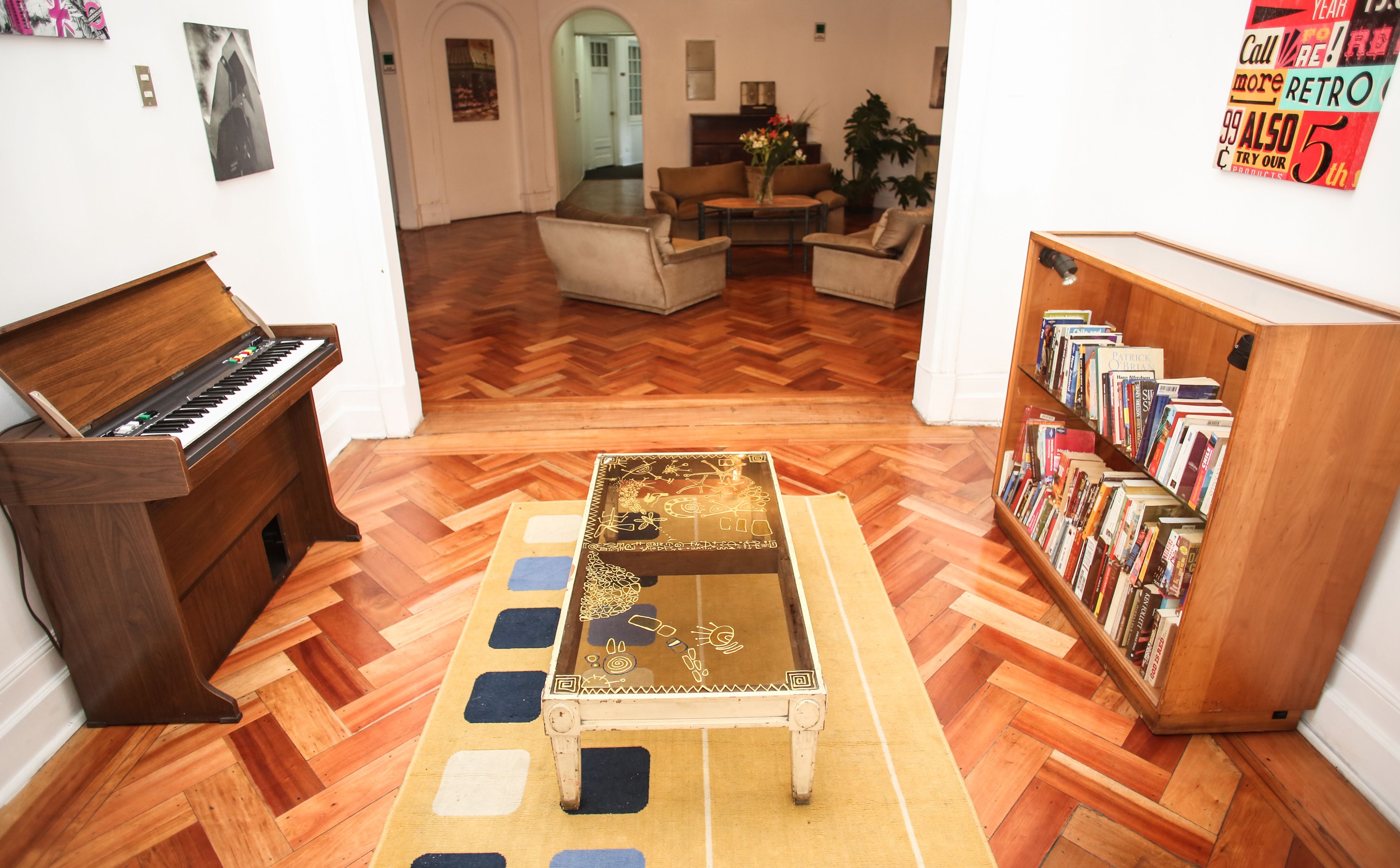 Uma sala de estar com um piano, uma mesa de centro com um tampo decorativo e uma estante repleta de livros.