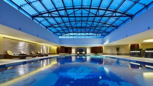 A large indoor swimming pool with a glass ceiling, lounge chairs, and a modern design. - Jin Jiang MingCheng Hotel (Yancheng)