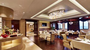 A restaurant with a central bar area, multiple dining tables, and a chandelier. - Jin Jiang MingCheng Hotel (Yancheng)