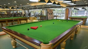 Eine Billardhalle mit mehreren Billardtischen, grüner Spielvlies und Deckenbeleuchtung.