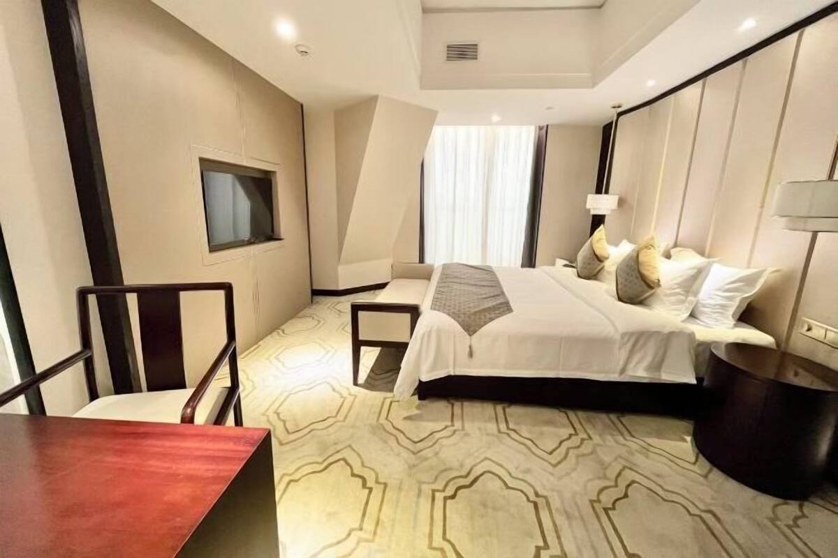 Habitación de hotel con cama, mesa, silla, lámpara y ventana.