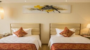 Ein Hotelzimmer mit zwei Betten, jeweils mit Kopfteil und einem dekorativen Kissen. Über den Betten hängt ein Gemälde.