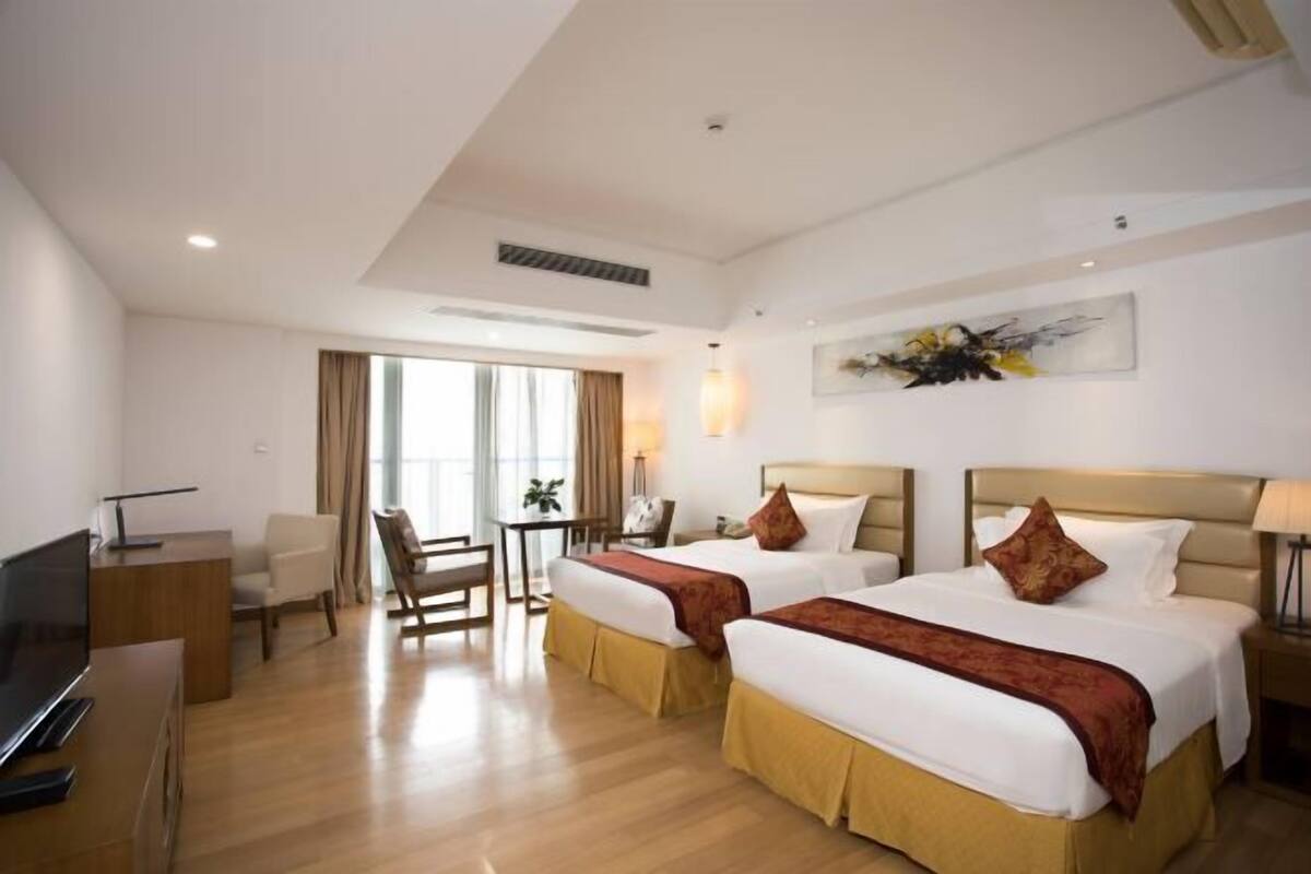Habitación de hotel con dos camas, un escritorio, un televisor y una ventana con cortinas.