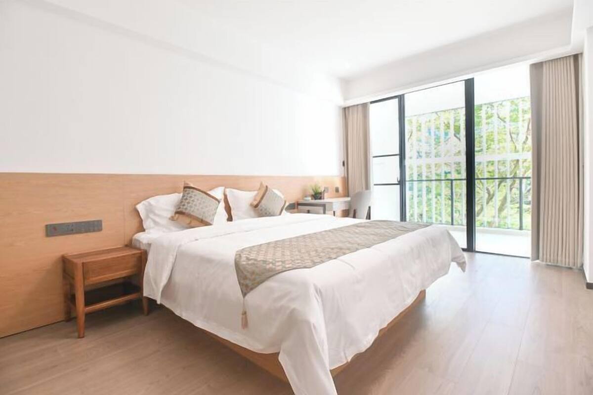 Una habitación de hotel con cama, mesita de noche, un escritorio pequeño y vistas amplias a través de grandes ventanales.