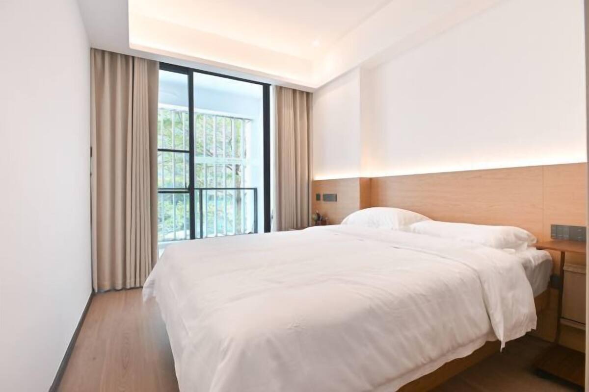 Habitación de hotel con una cama grande, cabecero de madera, ventana con cortinas y vistas a zonas verdes.