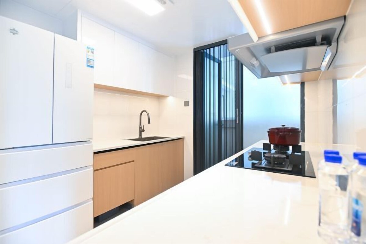 Une cuisine moderne avec des meubles blancs, un plan de travail noir, un évier, une cuisinière et une fenêtre équipée de stores verticaux.
