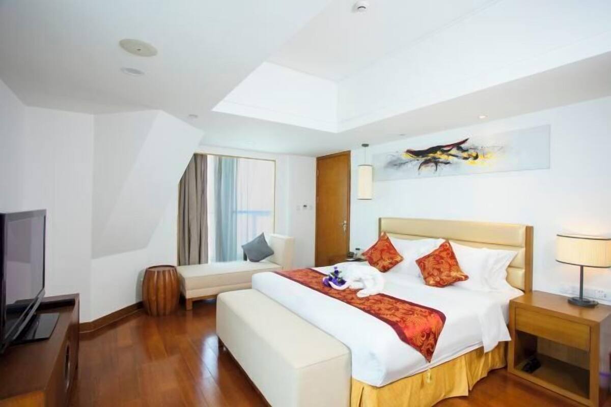 Habitación de hotel con cama, mesita de noche, lámpara, televisor y ventana con cortinas.