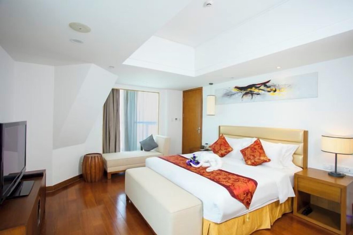 Une chambre d’hôtel avec un lit, une table de chevet, une lampe, une télévision et une fenêtre avec des rideaux.