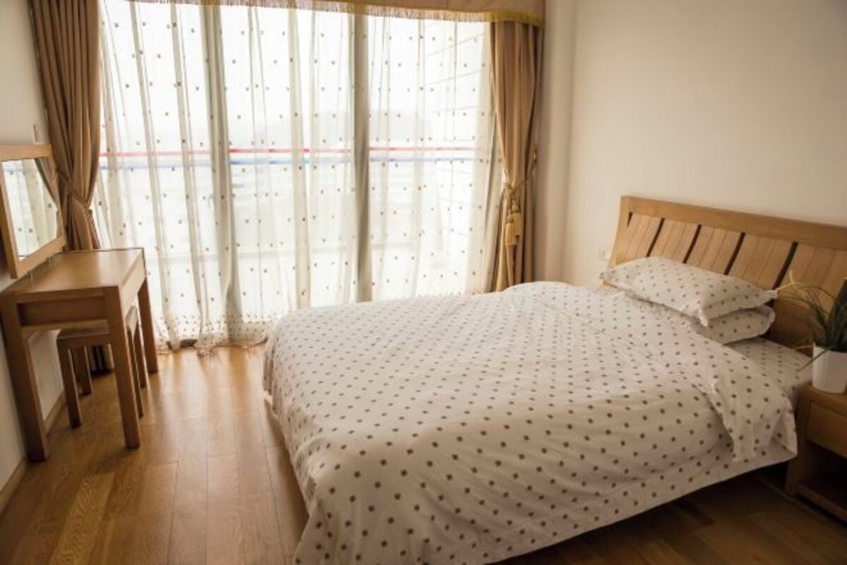 Une chambre à coucher avec un lit en bois, un bureau et une fenêtre avec des rideaux.