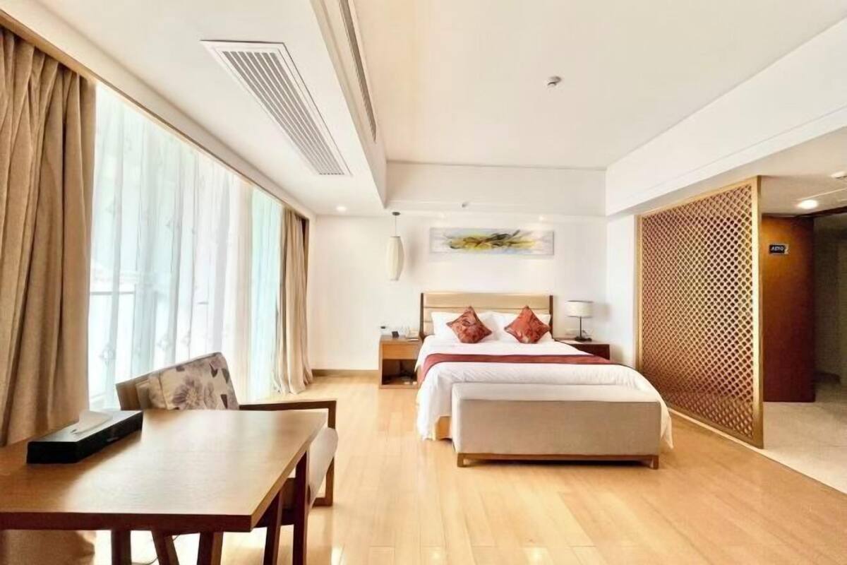 Habitación de hotel con cama, mesita de noche, lámpara y vistas a través de una ventana.
